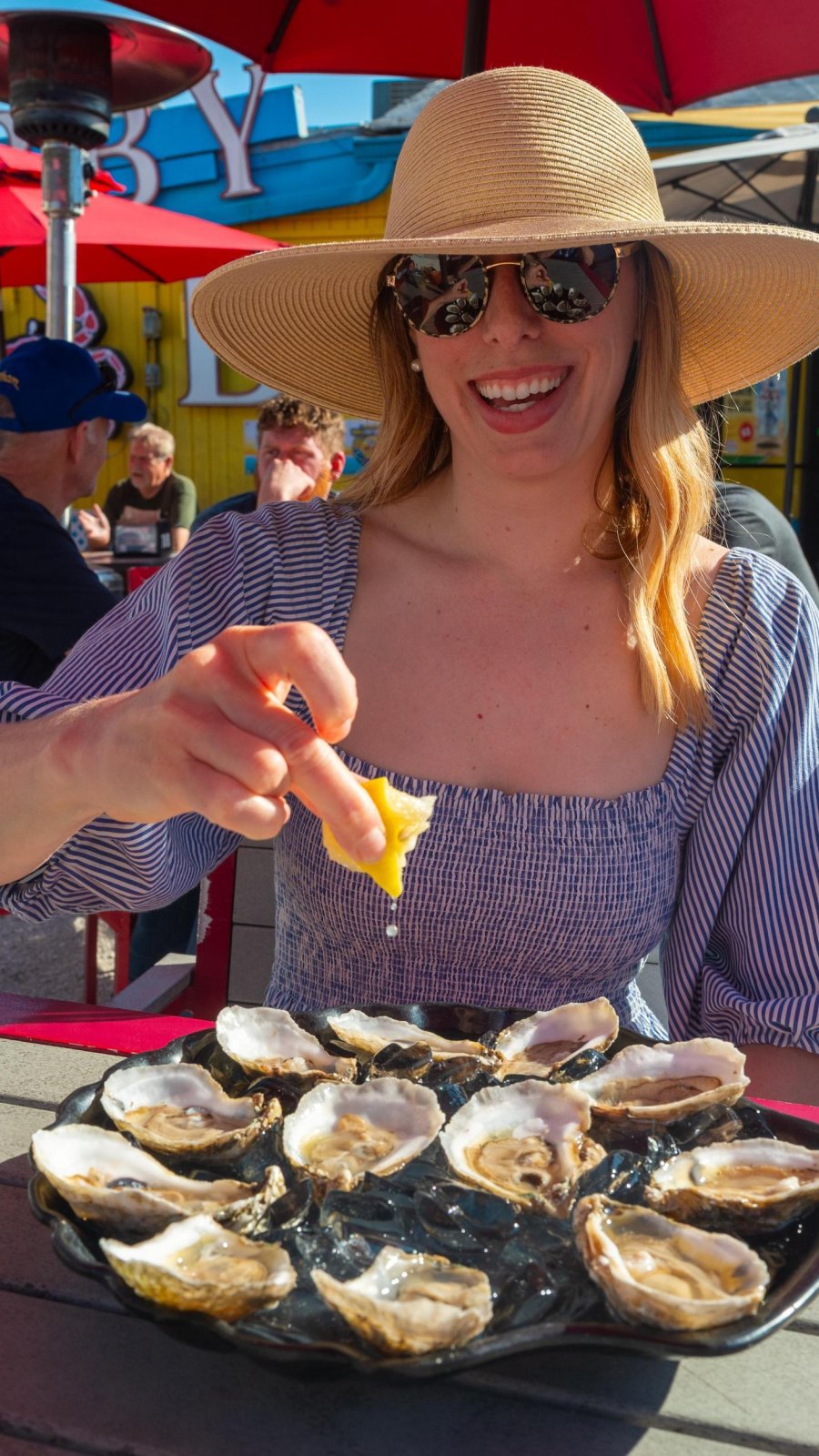 a woman squeezes a lemon over raw oysters while dining outside at The Original Crabby Bills