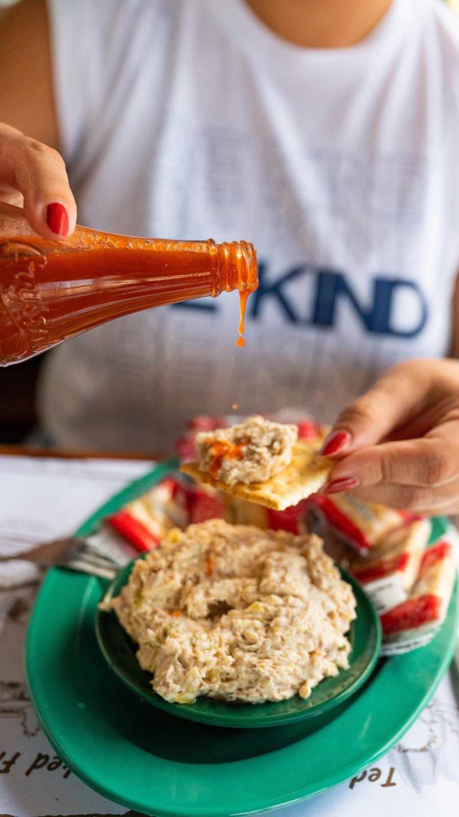 a woman putting hot sauce on a cracker with smoked fish dip at Ted Peters Famous Smoked Fish in St. Petersburg